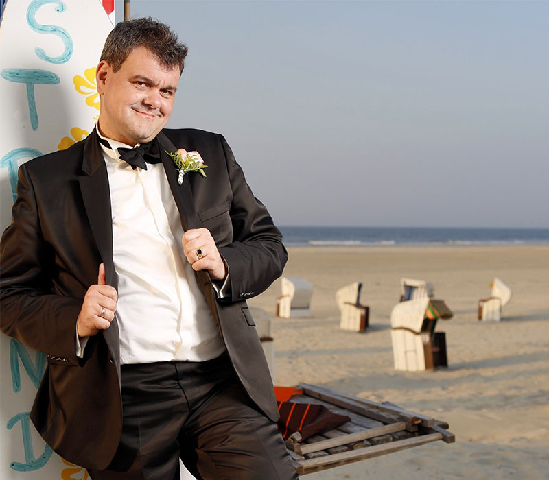 Hochzeitsbilder eines Mannes als Bräutigam im schwarzen Anzug am Strand in der Sonne