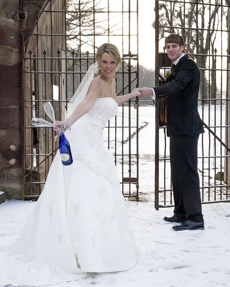 Hochzeitsfotografie von Brautpaar im Schnee mit Sekt am Tor