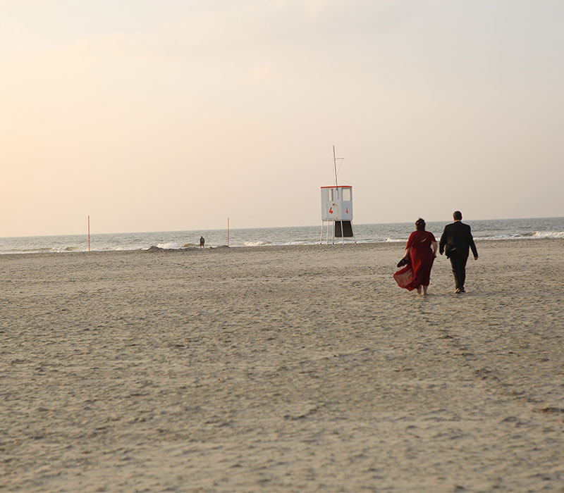 Hochzeitsbilder eines Paares am Strand, barfuß durch den Sand mit Sonnenuntergang am Horizont